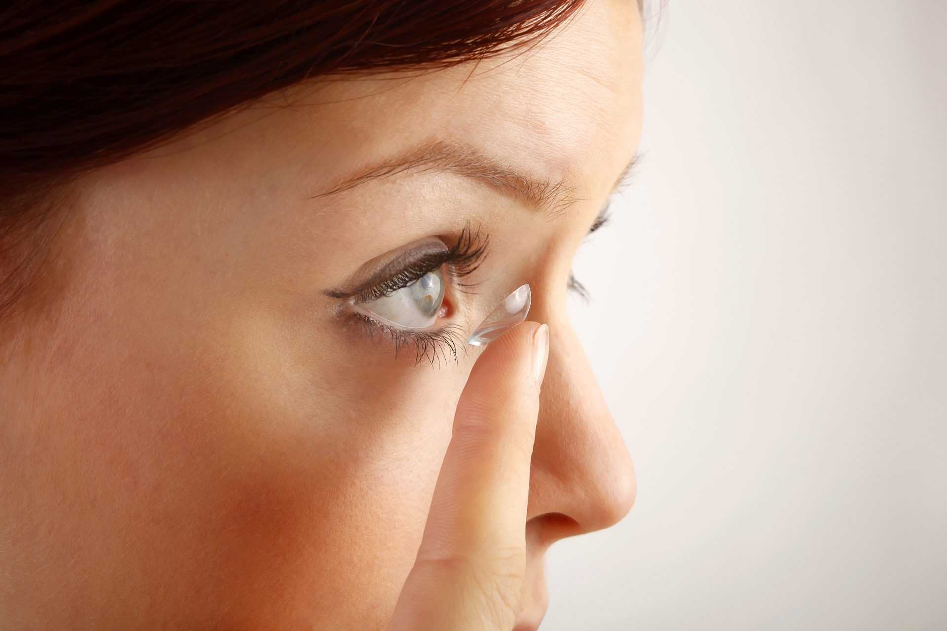 Kontaktlinse auf der Fingerspitze vor einem Auge