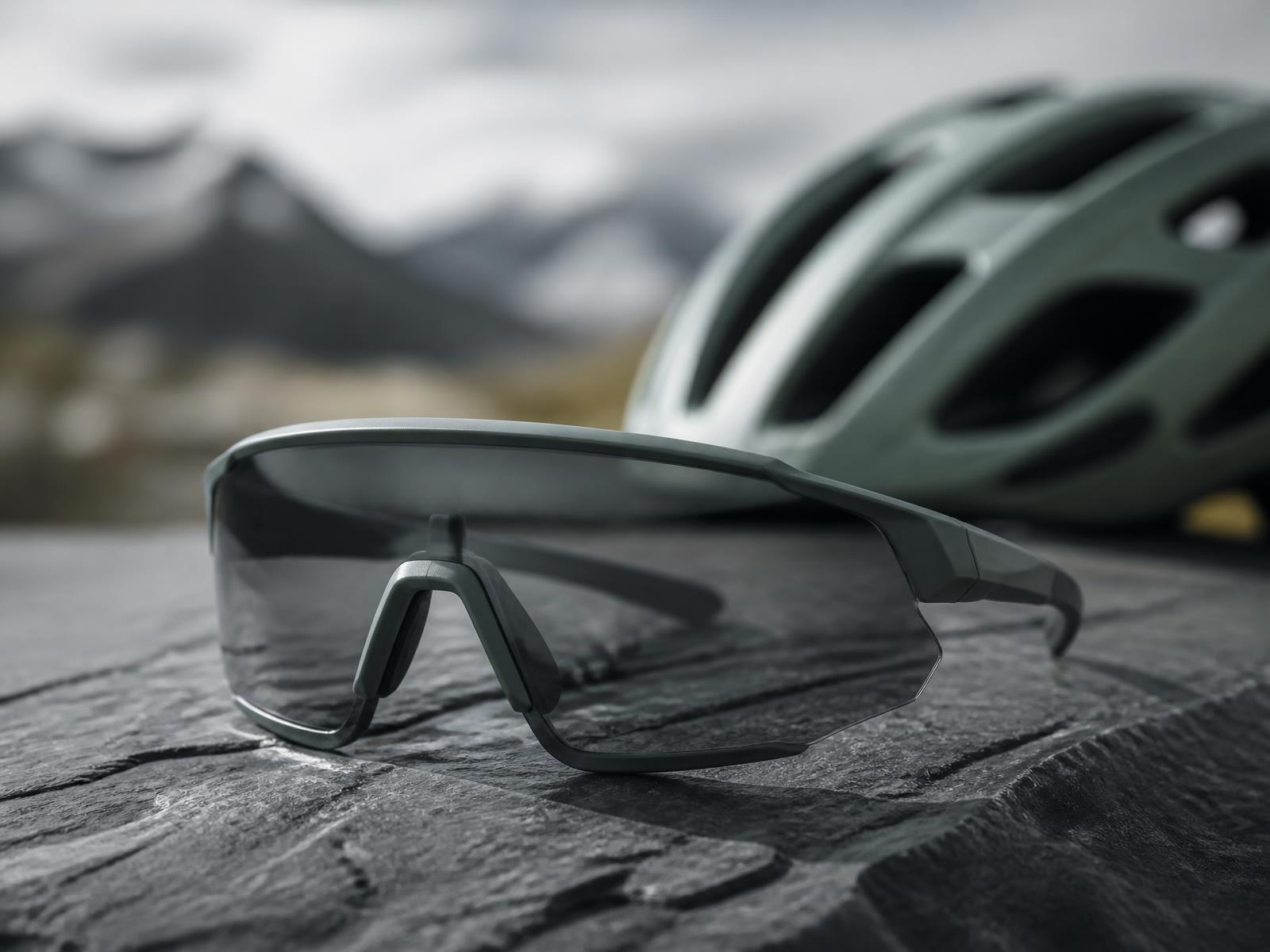 Sportbrille mit durchgehendem Glas auf einem Stein, dahinter ein Fahrradhelm